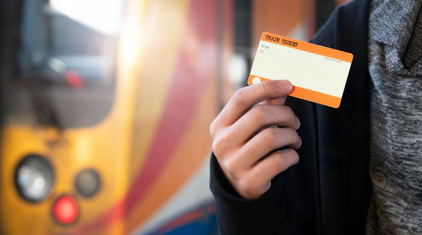 A passenger holding a train ticket with a yellow train in the background