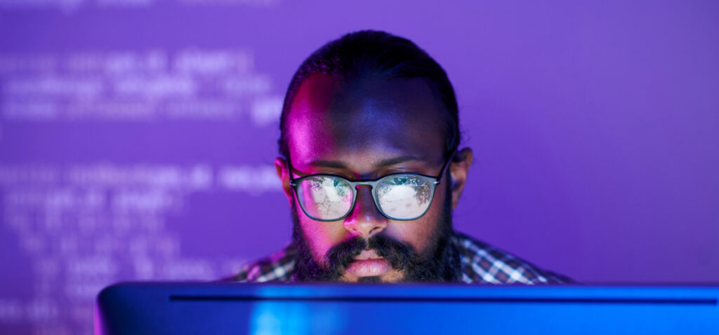 A man with glasses, reading lines of code on a computer