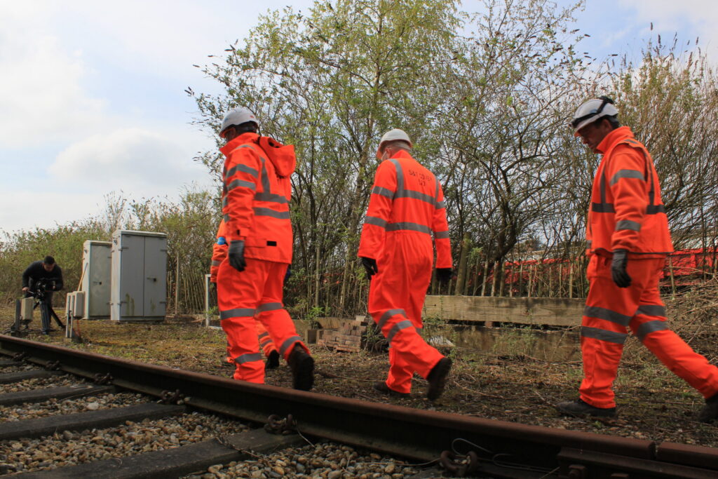 An image of three people working on a railway line in red high visibility clothing