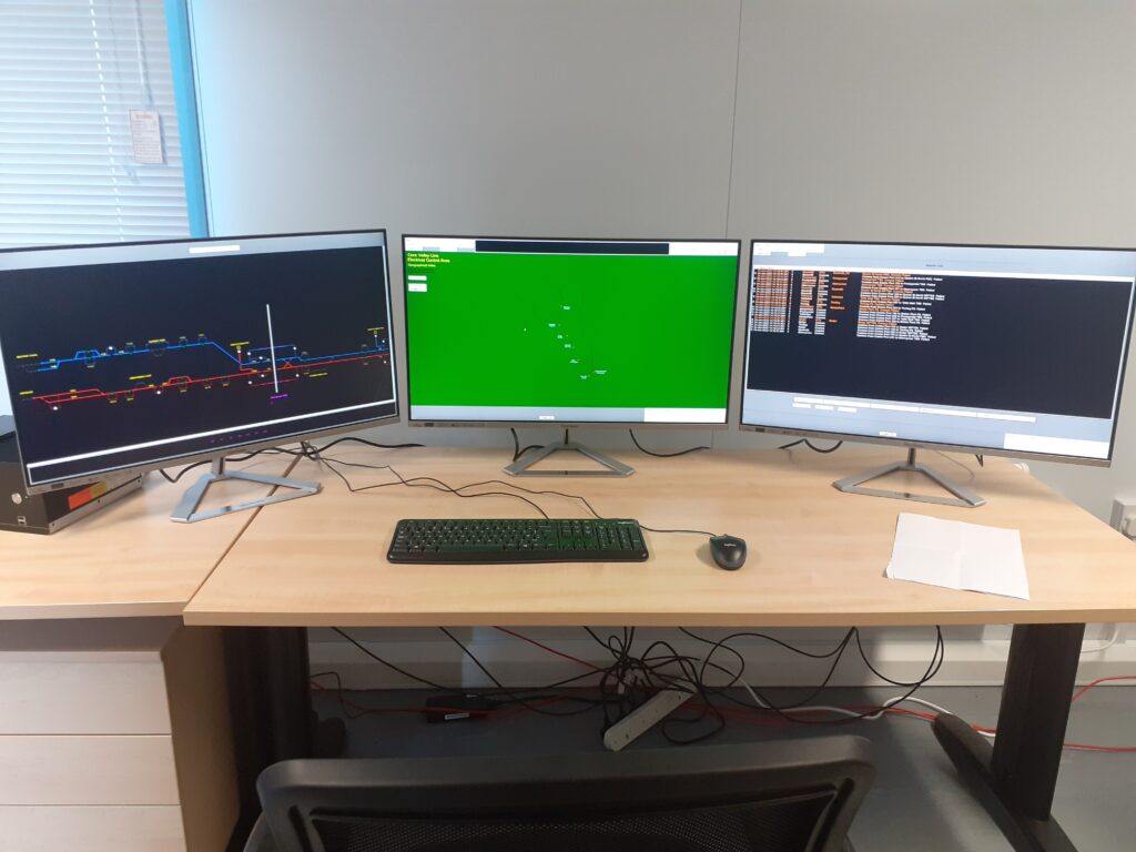 Three computer screens showing various numbers and formulas on a desk