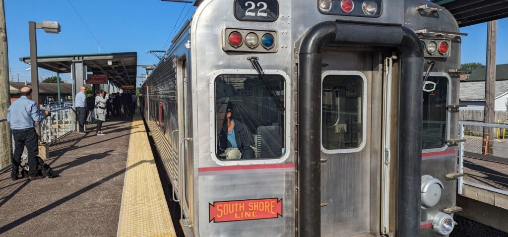 The front of a silver commuter train at a train stop