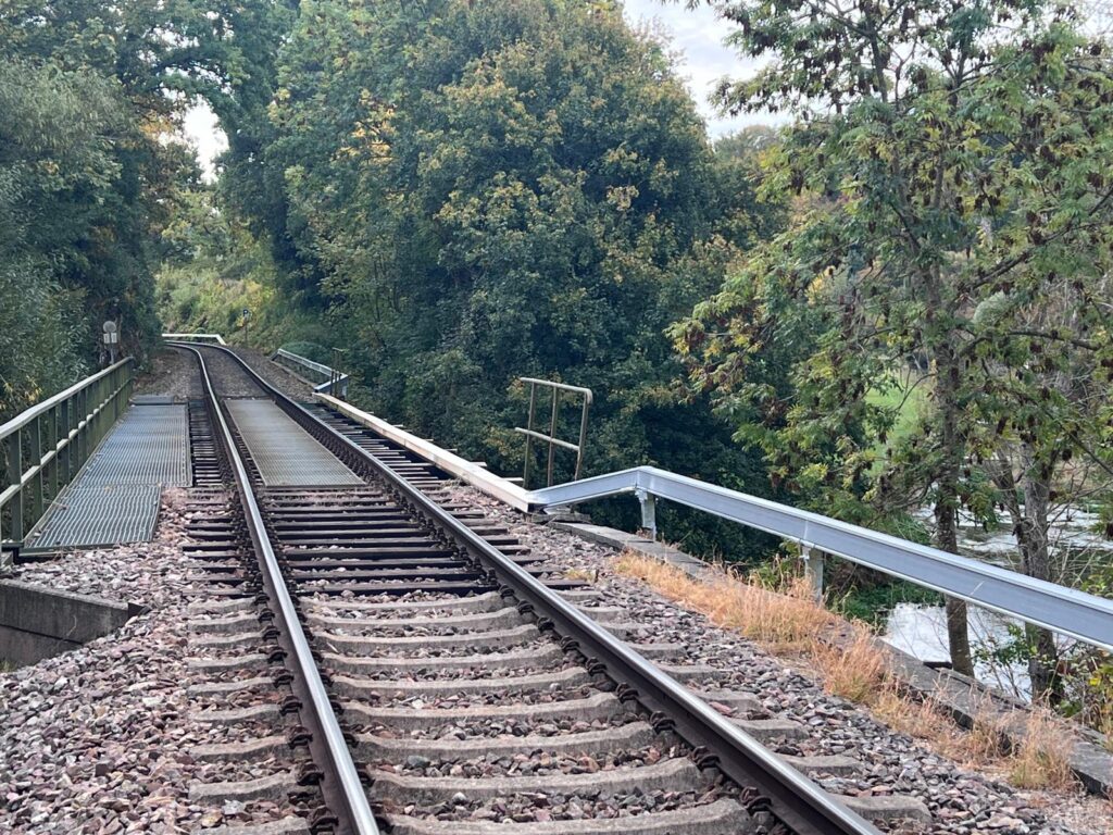 A train track on a bridge with a silver arcosystem cable management system next to it