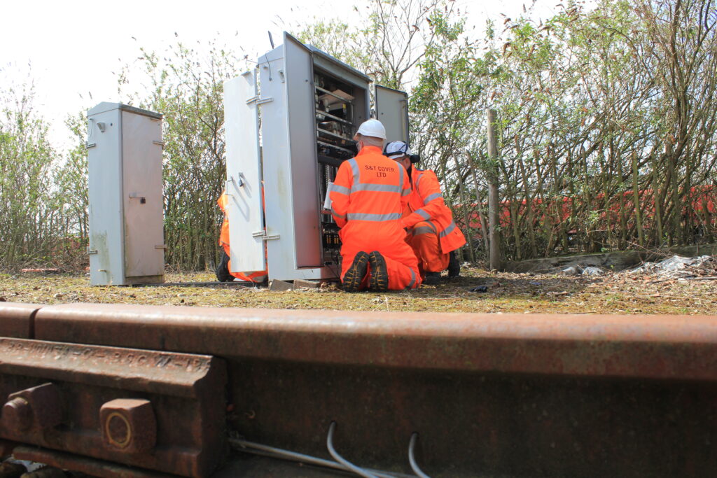 workers in front of an electrical box beside a railway track