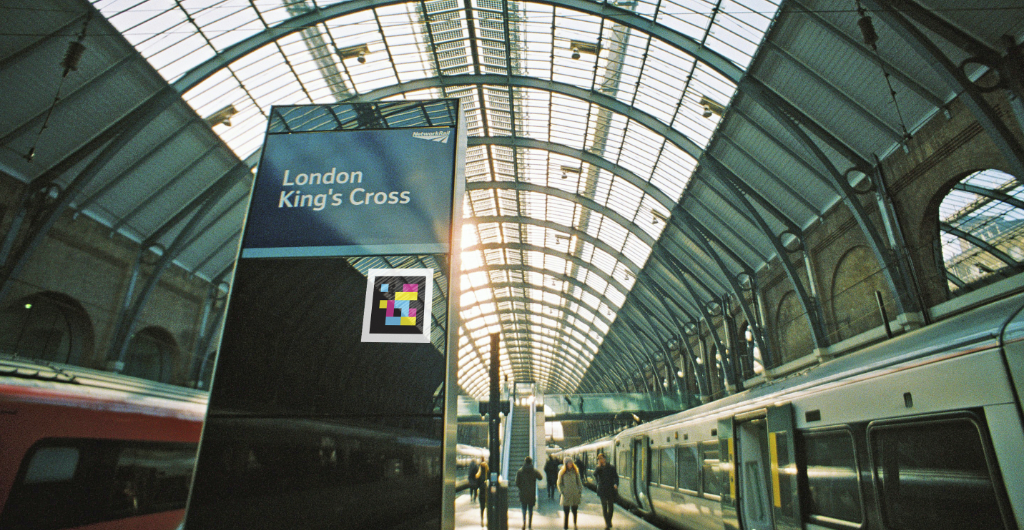 Inside a domed building with windows on the ceiling, there are trains either side of a walkway and a large sign centre frame reading "London King's Cross"