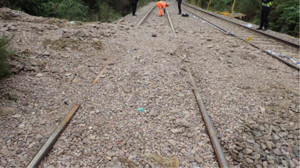 Workers investigate a rail track which is covered in rocks, mud and debris