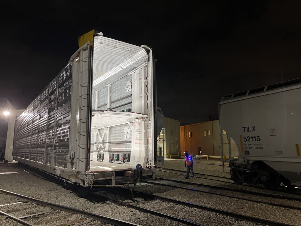 A railcar is pictured at a railyard. A bright white light illuminates the inside of the railcar to show 2 levels for car storage