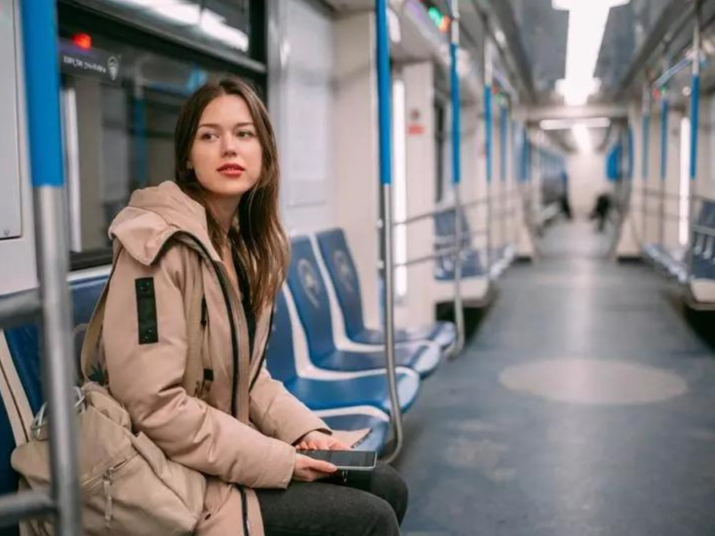 A woman in a beige coat is sat on an empty train car at night
