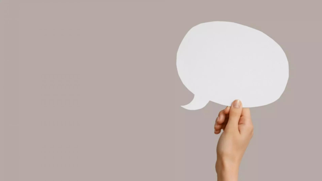 A white paper speech bubble is being held up by a hand. The background is beige