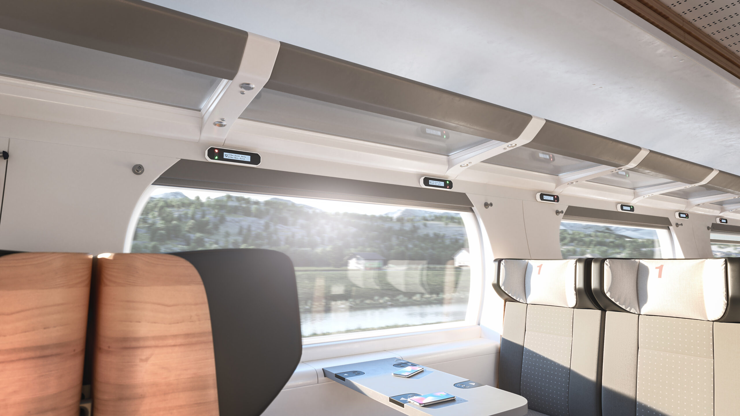 Interior of a modern first-class train carriage with spacious seating, large windows showing a scenic countryside view, overhead luggage racks, and individual digital seat reservation displays.