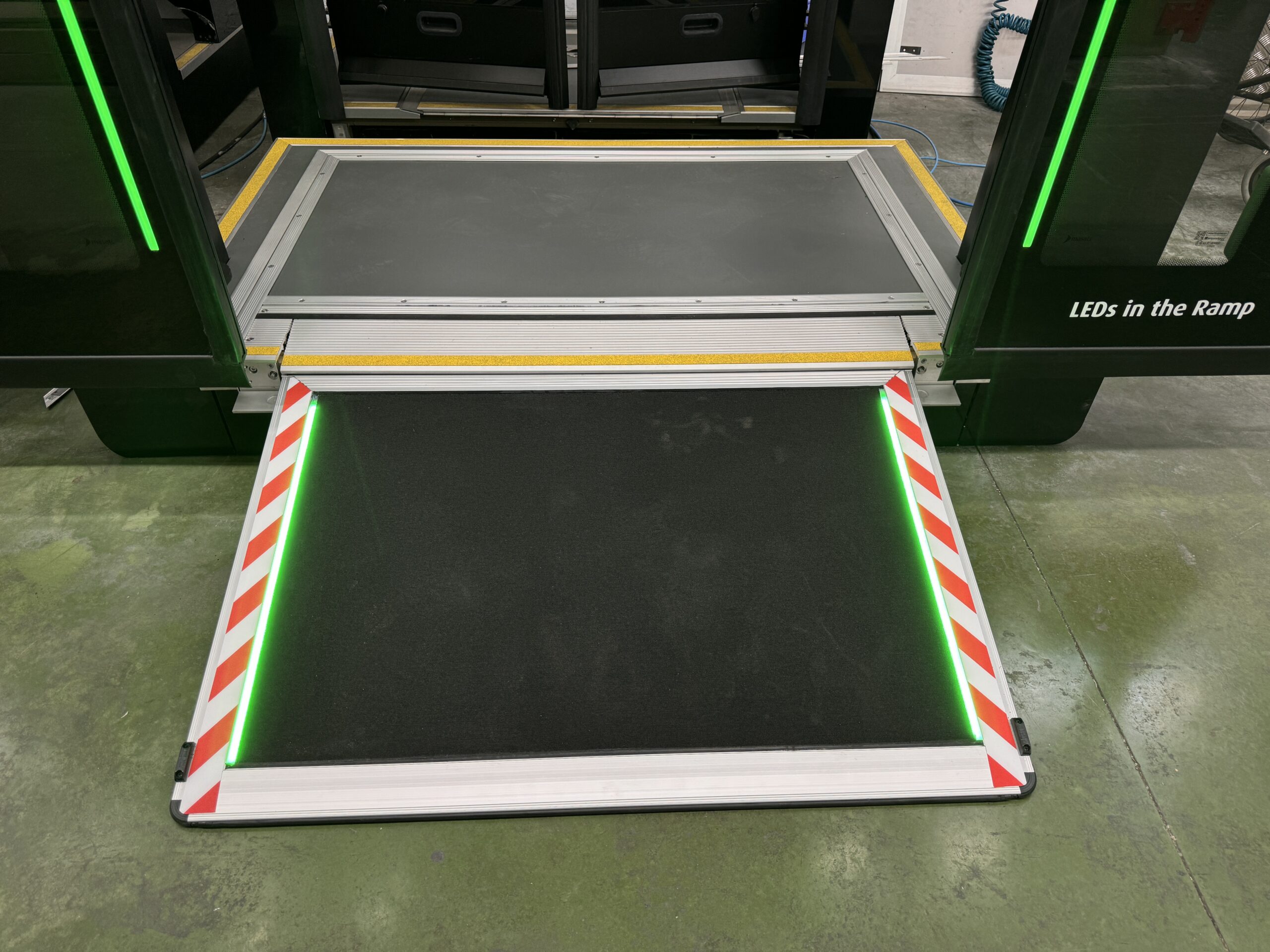 A close-up of a red city bus with its accessibility ramp extended onto the pavement, showing interior space designated for wheelchair users and other passengers with mobility needs.