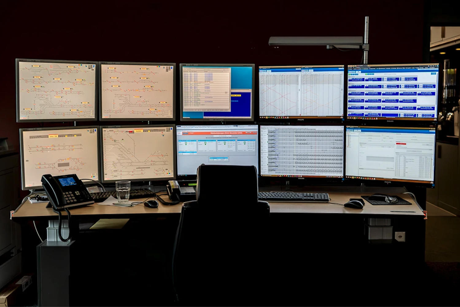 A comprehensive view of a control room featuring a desk with a phone and a chair, facing eight large monitors displaying complex data and schematics.