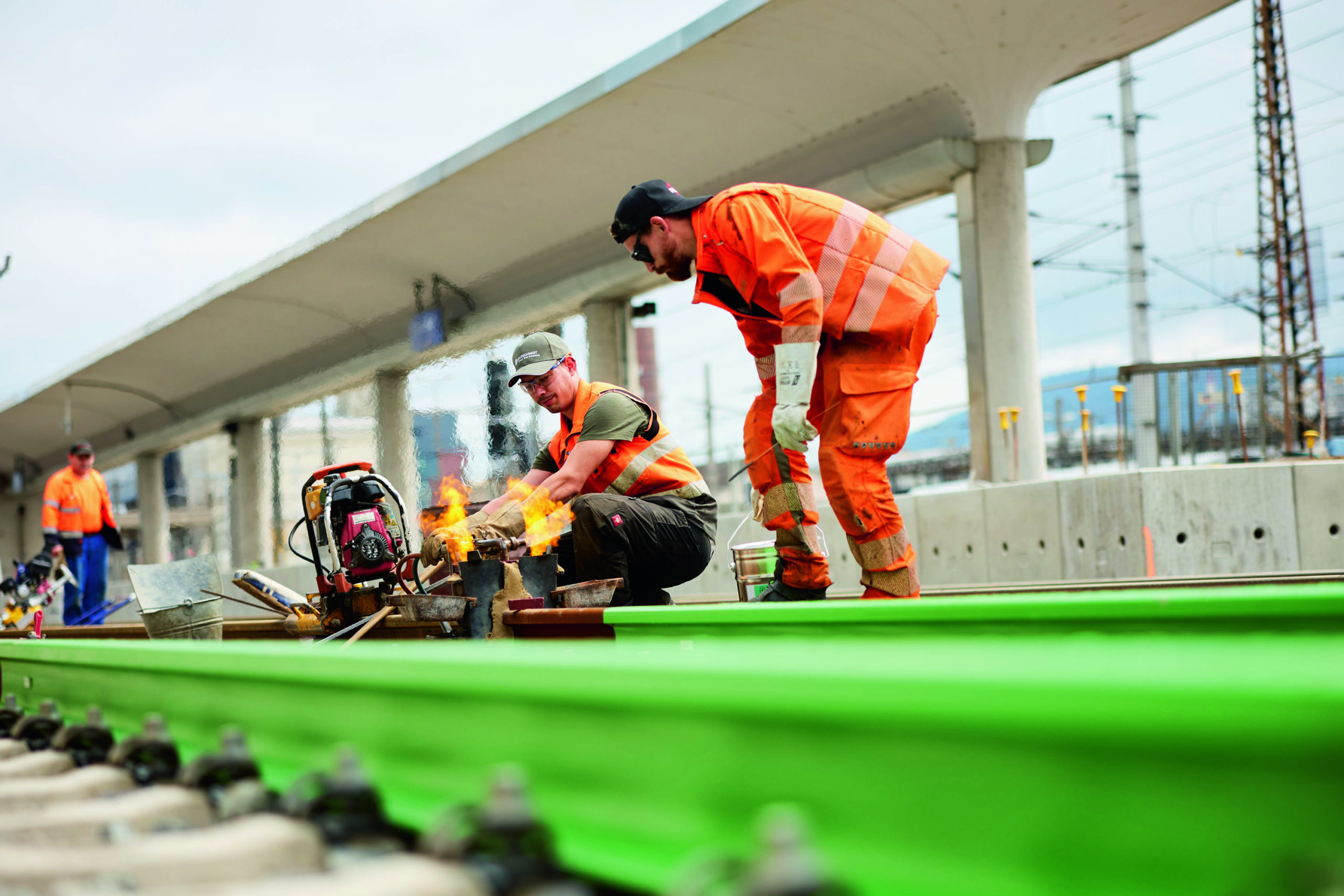 Workers in orange outfits working on a green rail track