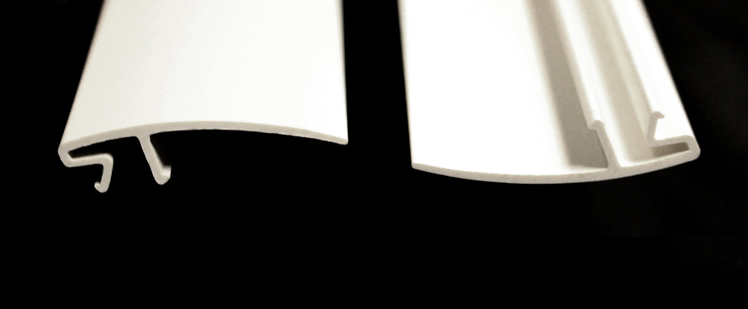 Two curved white plastic extrusions are shown, one with a complex internal profile and the other with a simpler C-channel shape.