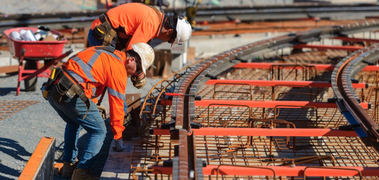 Rail workers in orange vests work on a section of track