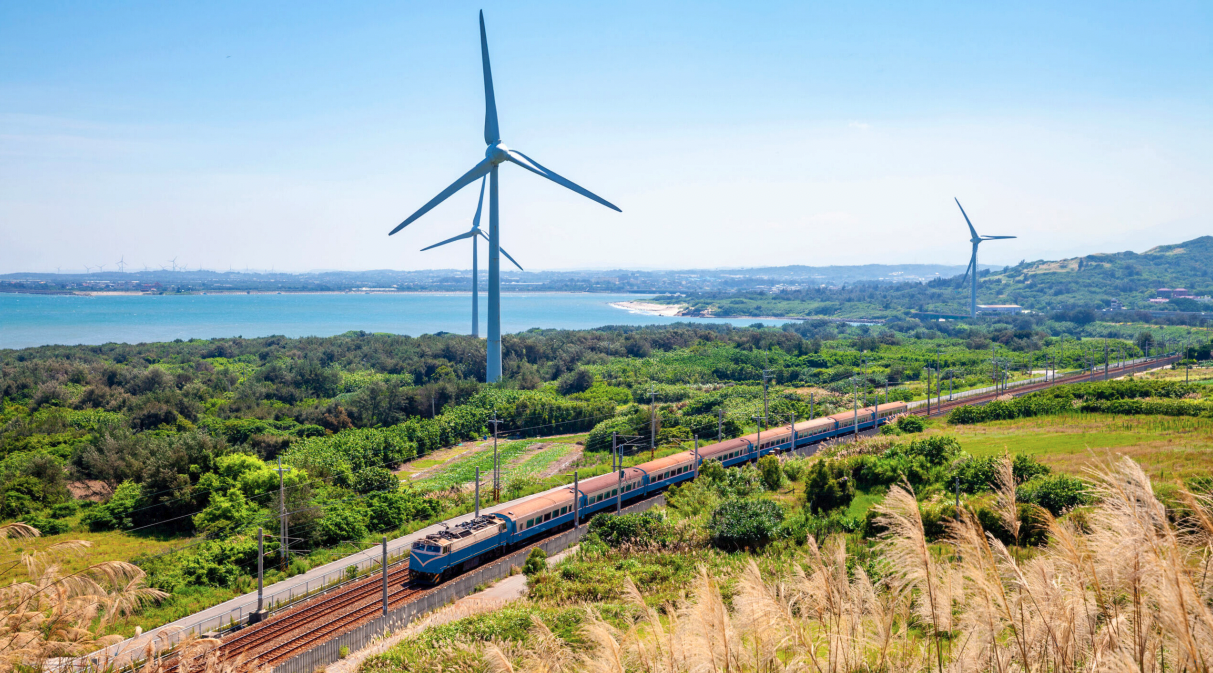 A cargo train travelling through the countryside, wind turbines in the background