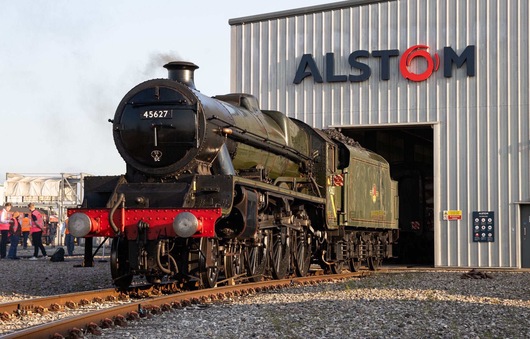 A black and red steam train leaving an Alstom showroom