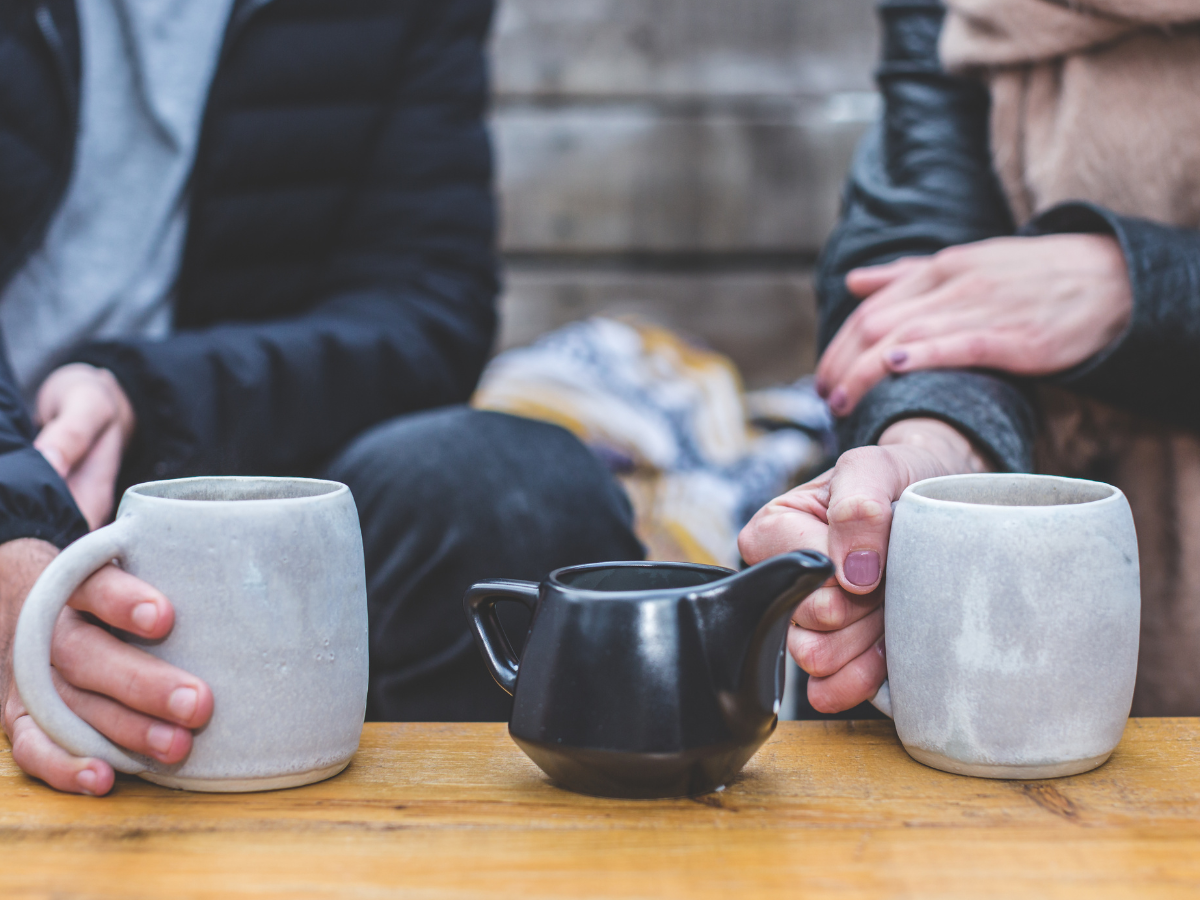 Two people having a conversation with mugs and a teapot