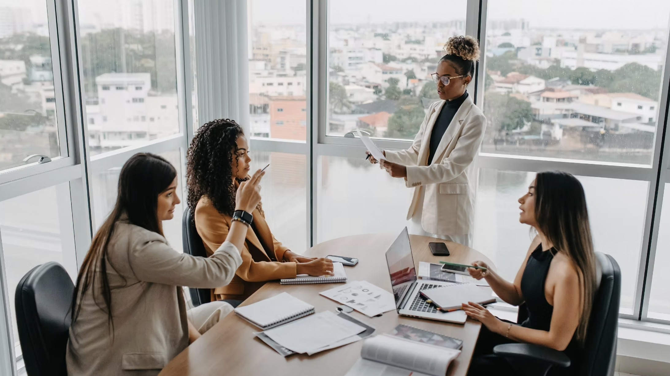 Four women sat around a table in a high-rise office building, conducting a meeting