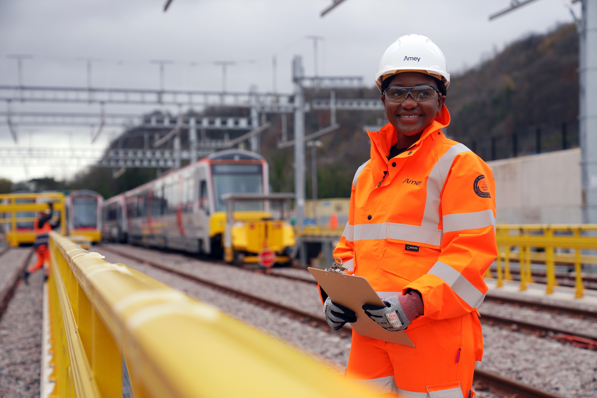 A woman smiling in high-vis by a train platform