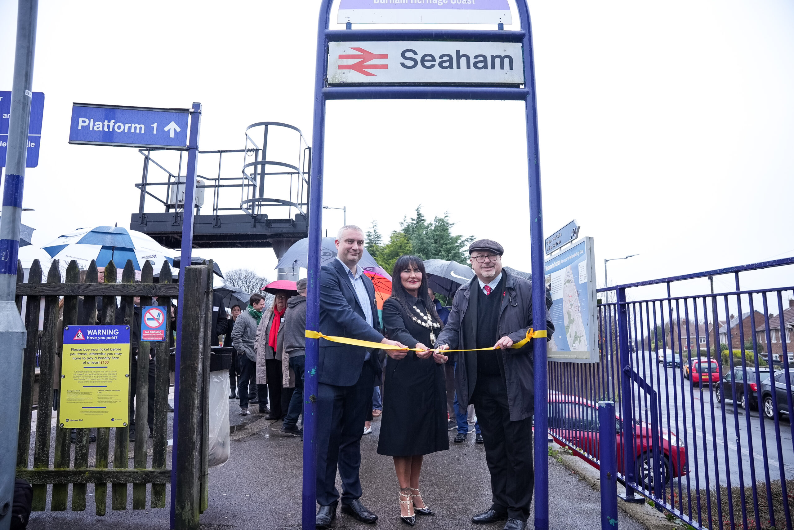 Three people cutting the ribbon on a gate