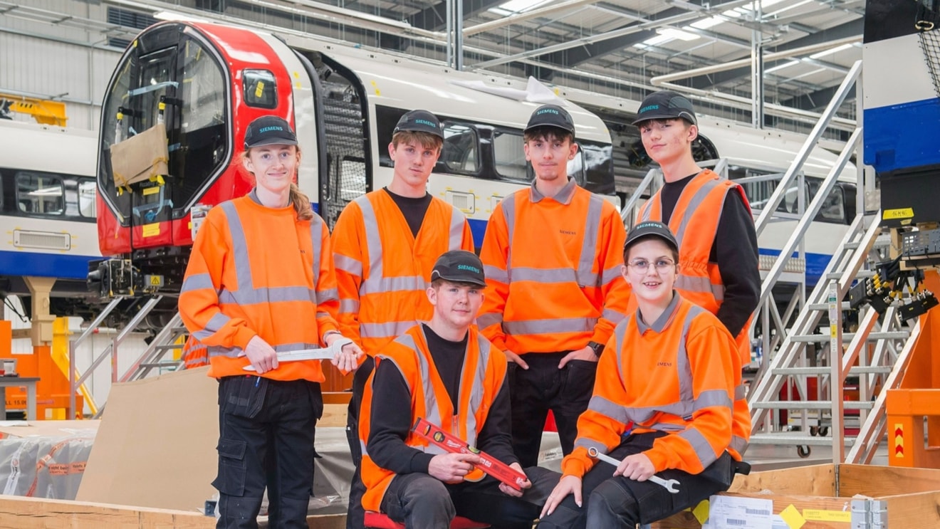 A set of young people in orange hi vis in front of a train