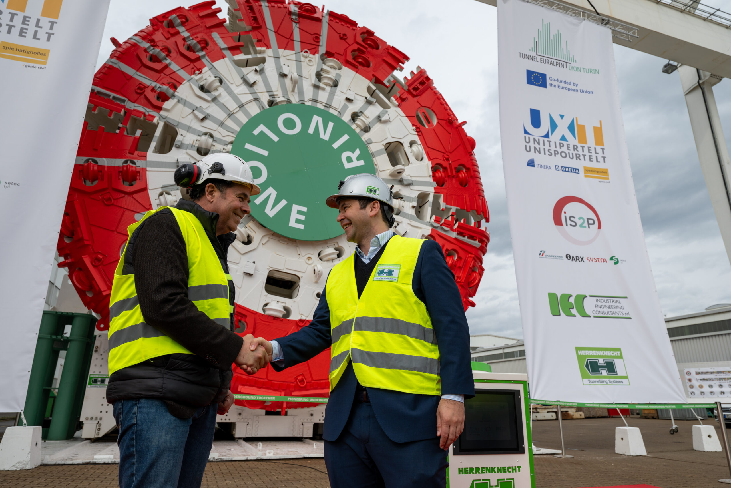 Two men shaking hands in front of a large tunnel boring machine