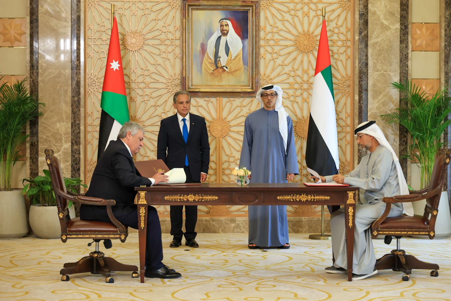 Two men signing contracts at a long table whilst two other men watch on