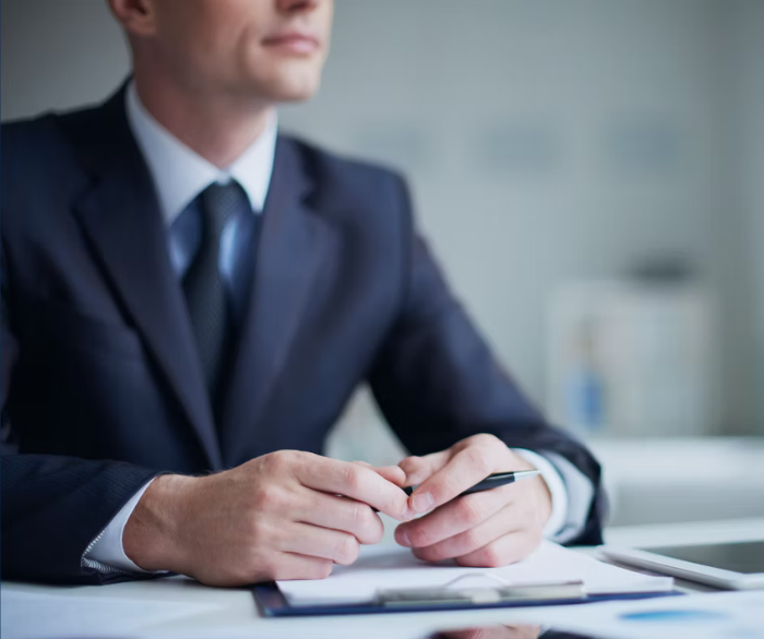 Man dressed in business suit sat down holding a pen