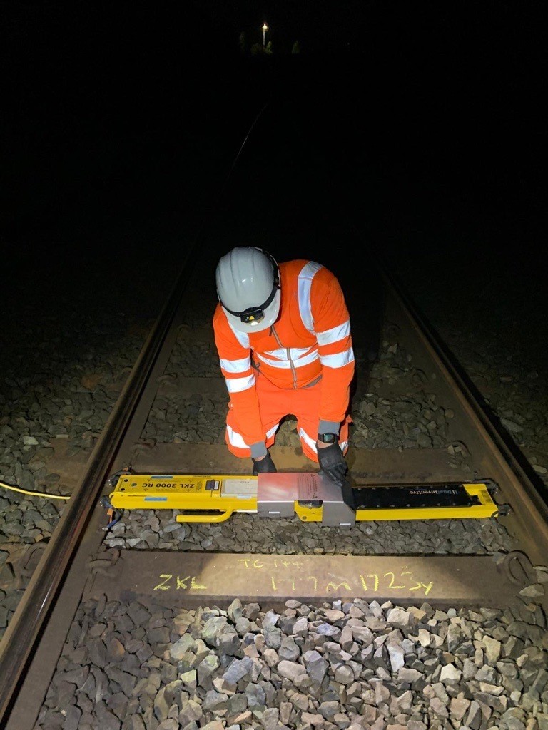 Close-up of a track worker installing a Dual Inventive ZKL 3000 RC device on the rail at night