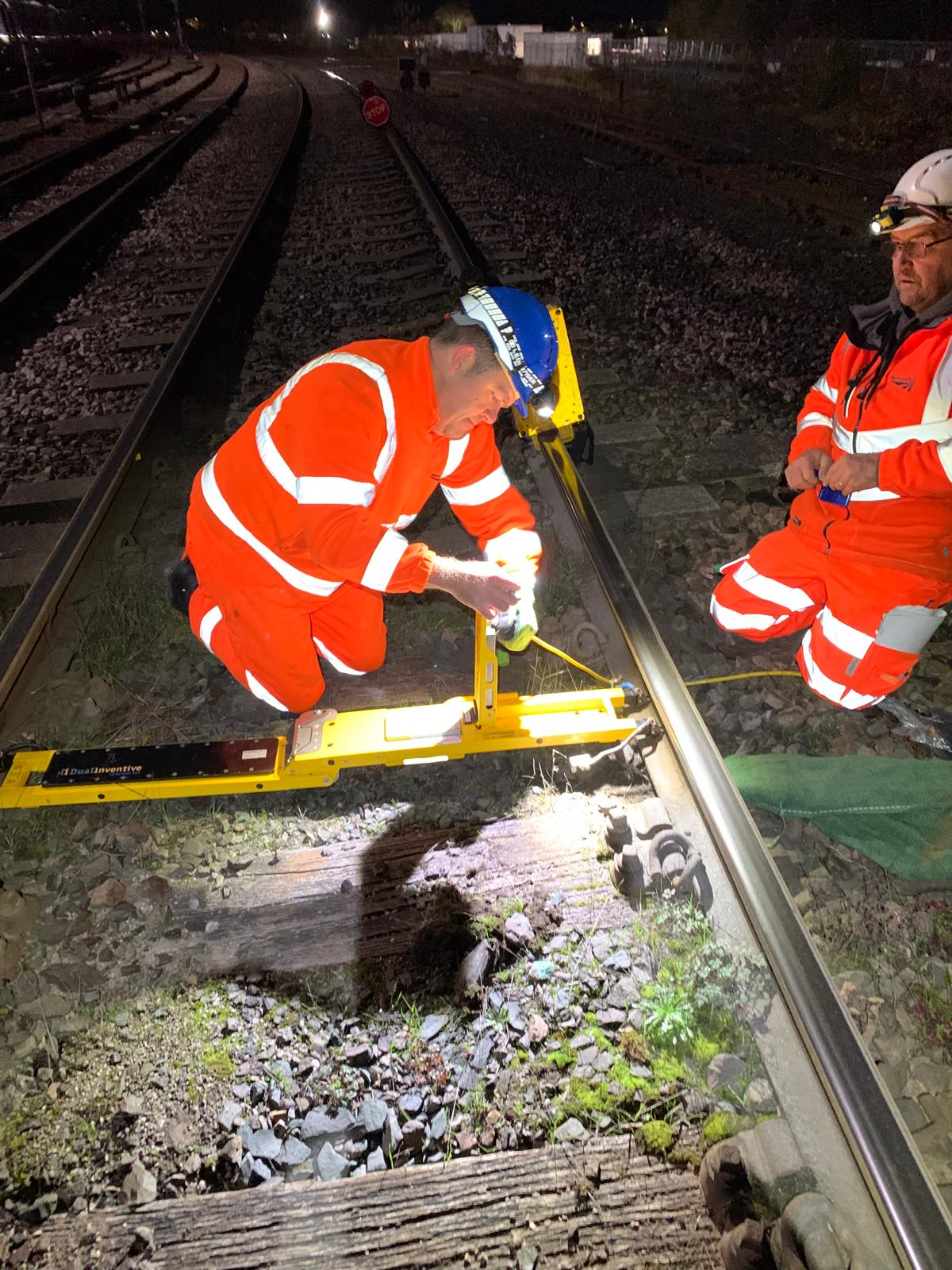 Track workers installing a Dual Inventive ZKL device on the rail at night
