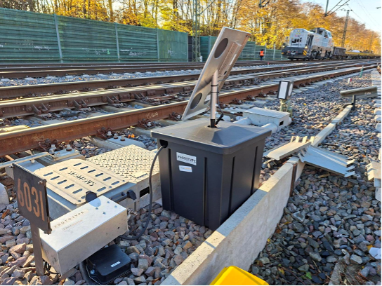 RSS 3000 PC unit installed trackside near a point number marker, with a rail vehicle passing in the background