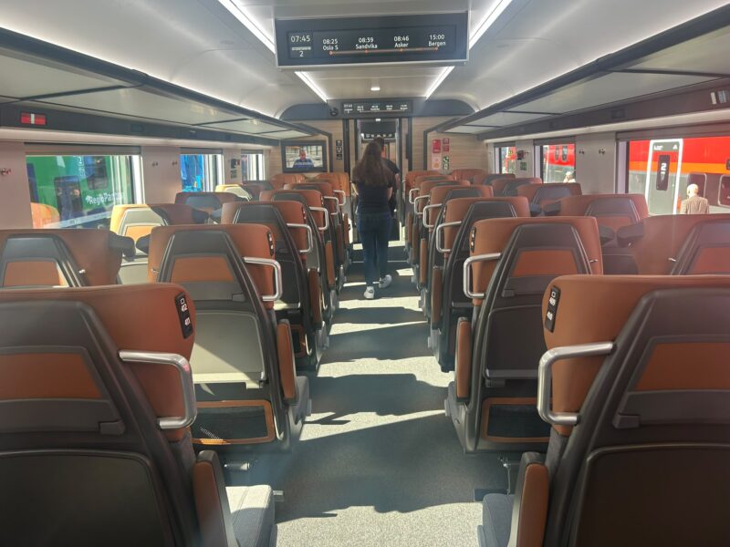 The standard seating area of the FLIRT Nordic Express. The overhead passenger information screen displays a sample Oslo S–Bergen journey via Sandvika and Asker, one of the long-distance routes the train is designed for