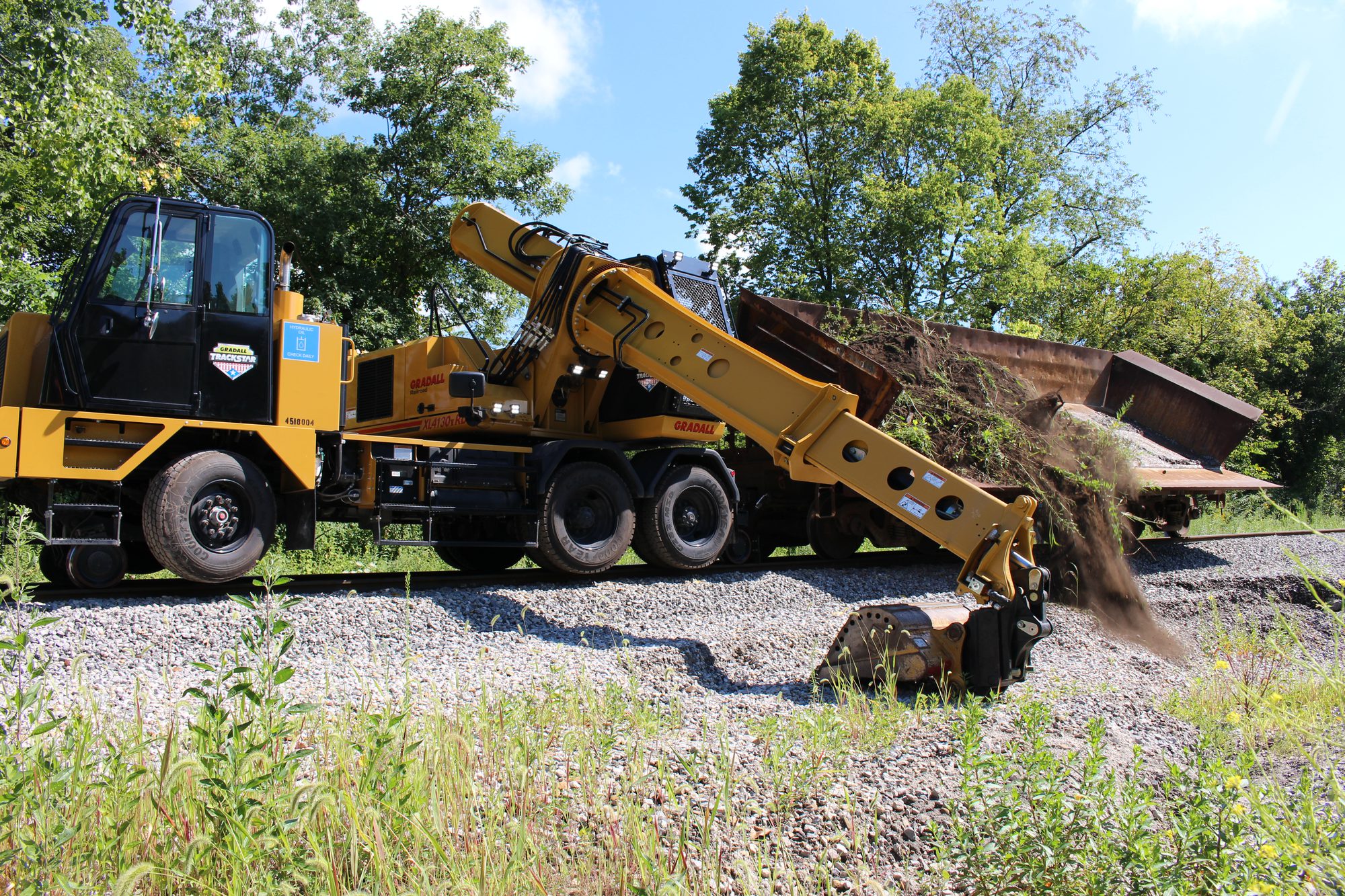Gradall TrackStar XL 4130 V highway speed road-rail excavator casting spoil beside the track while coupled to a wagon