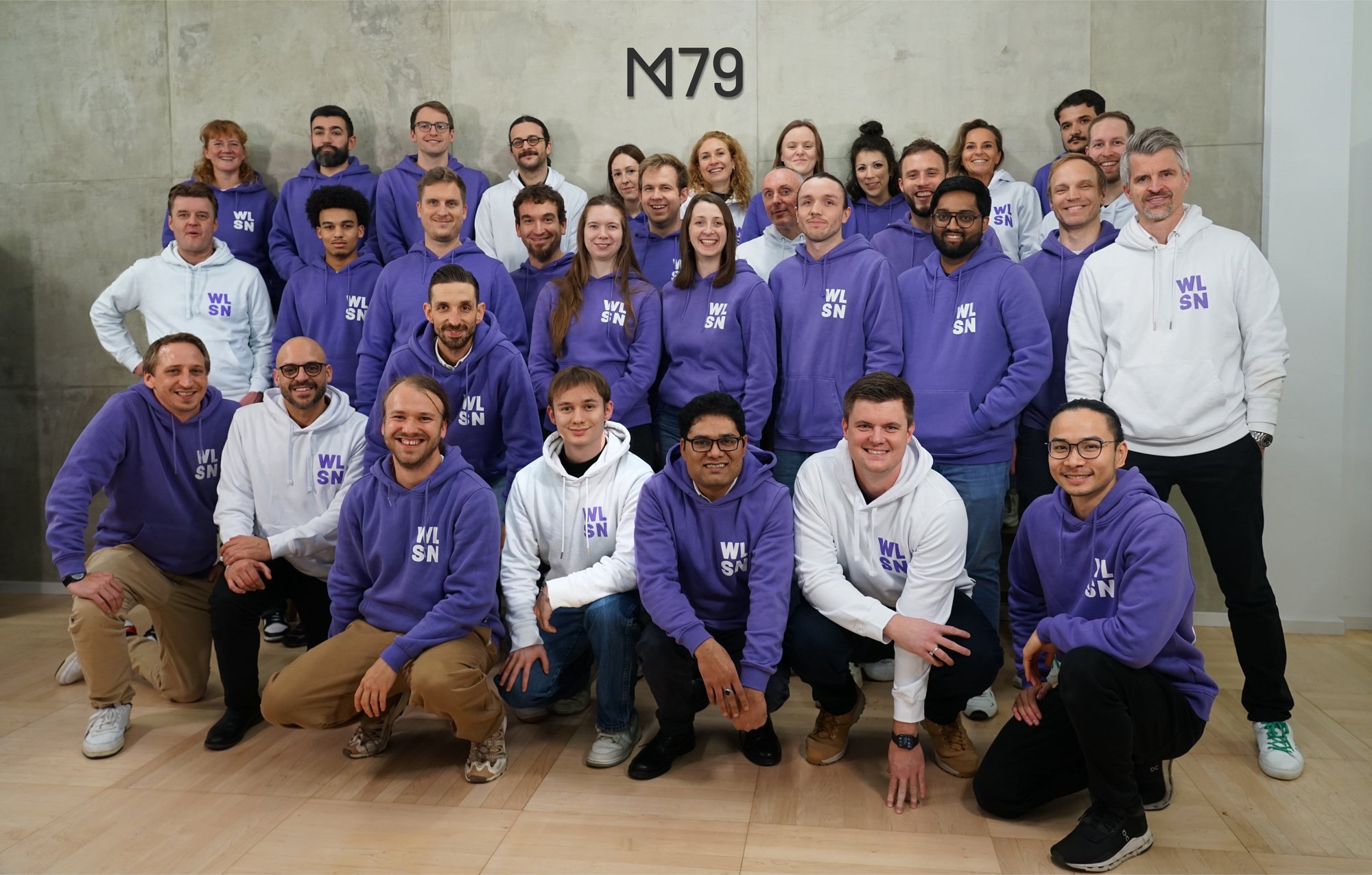 The Menlo79 team, around thirty people in branded hoodies in front of a concrete wall