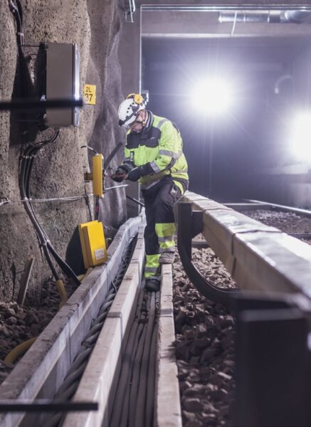Engineer in high-visibility clothing working on trackside signalling equipment in a Helsinki Metro tunnel