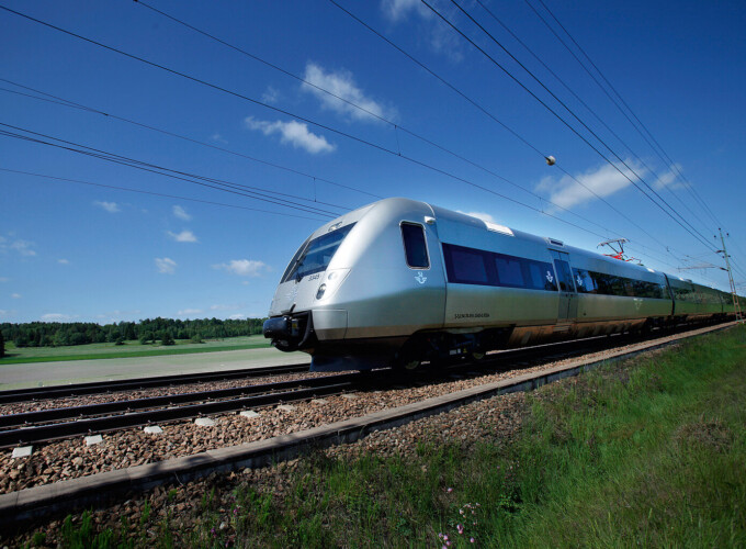 SJ 3000 train travelling through open Swedish countryside on an electrified line under clear skies