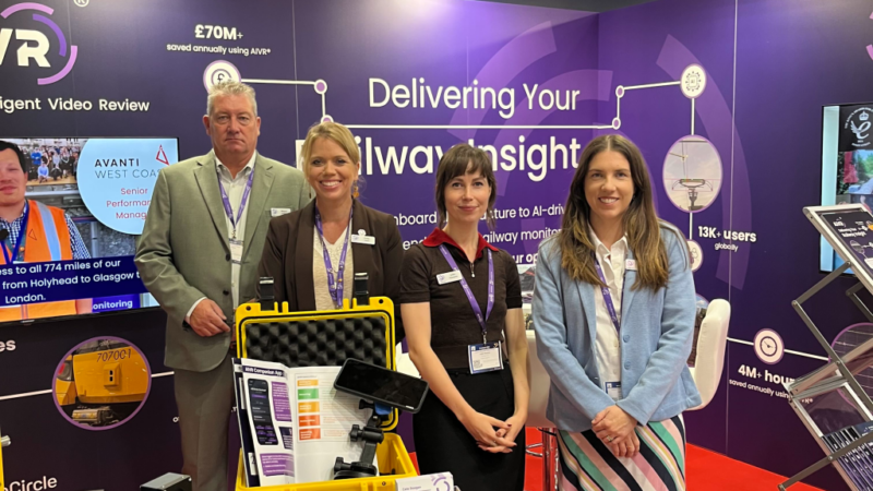 Four members of the One Big Circle team standing on their purple AIVR stand at InnoTrans 2026 in Berlin, beside a yellow equipment case and AIVR Companion App leaflets, with "Delivering Your Railway Insight" graphics behind them