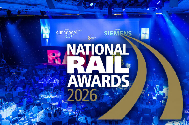 National Rail Awards 2026 logo with a gold curved track motif over a blue-lit banqueting hall set with round dinner tables, marking One Big Circle's shortlisting in two categories for its AIVR overhead line monitoring work