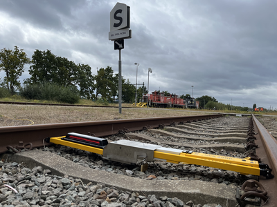 Dual Inventive RCS 3000 mobile signal mounted across railway track at a marshalling yard, with a red locomotive in the background