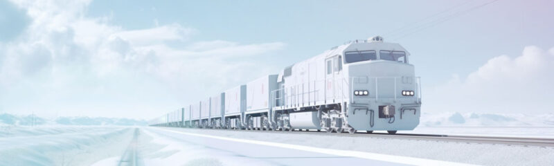 White freight locomotive with a front-mounted Rail Vision sensor unit hauling a long train of wagons through a snowy landscape