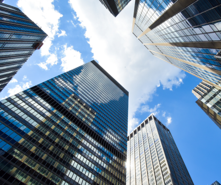 Looking up at tall glass skyscrapers against a bright blue sky with white clouds