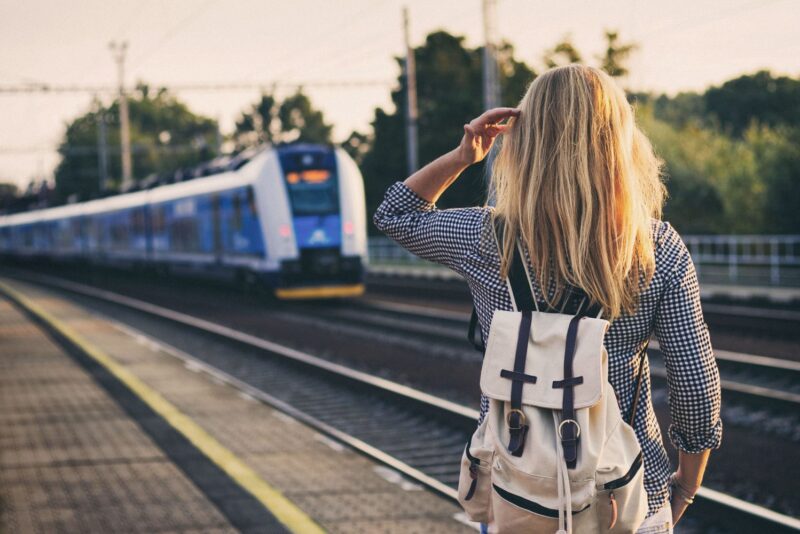 Passenger with a backpack waiting on a station platform as a blue and white train approaches